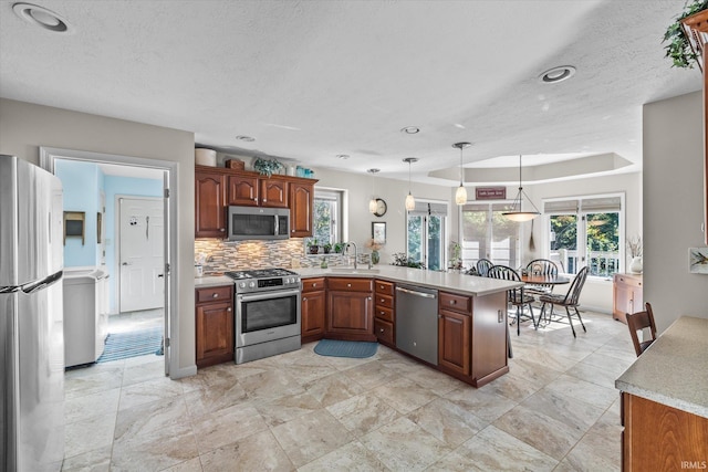 kitchen with decorative light fixtures, tasteful backsplash, kitchen peninsula, sink, and appliances with stainless steel finishes