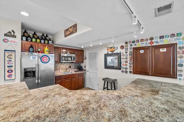 kitchen featuring kitchen peninsula, backsplash, stainless steel appliances, and a textured ceiling