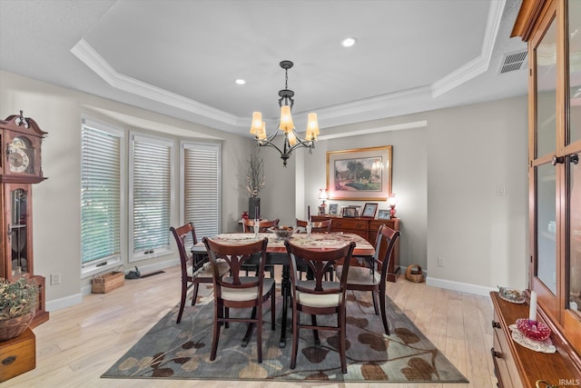 dining room with an inviting chandelier, crown molding, light hardwood / wood-style floors, and a tray ceiling