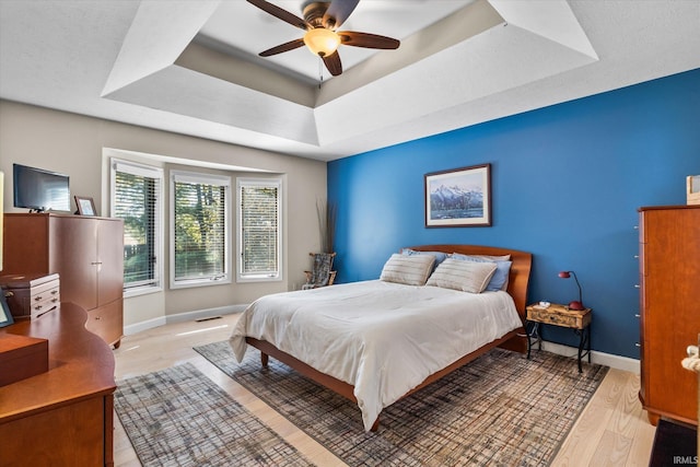 bedroom featuring ceiling fan, a tray ceiling, and light hardwood / wood-style flooring