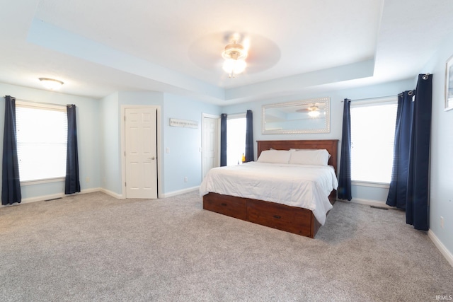 carpeted bedroom featuring ceiling fan, a raised ceiling, and multiple windows