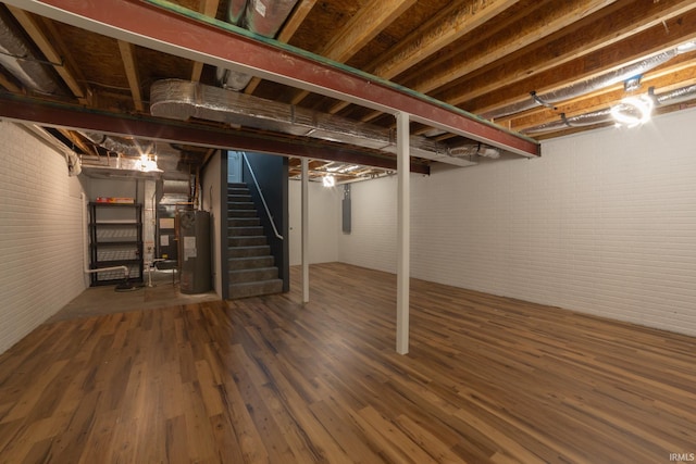 basement with dark hardwood / wood-style floors, electric panel, electric water heater, and brick wall