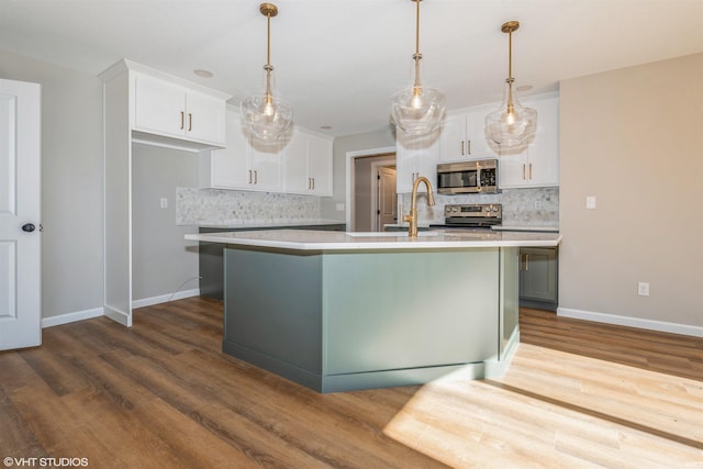 kitchen featuring decorative light fixtures, white cabinets, stainless steel appliances, and an island with sink