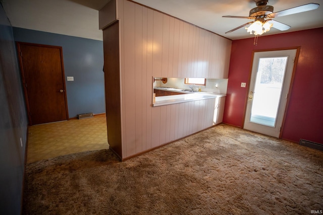 kitchen featuring ceiling fan, light colored carpet, and wood walls