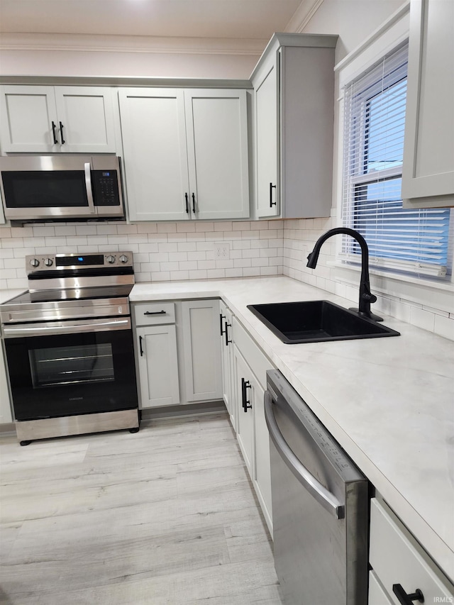 kitchen featuring stainless steel appliances, decorative backsplash, sink, light hardwood / wood-style floors, and light stone counters