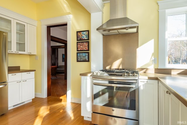 kitchen featuring white cabinets, stainless steel gas range oven, island range hood, and light hardwood / wood-style flooring