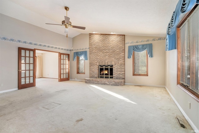 unfurnished living room with ceiling fan, vaulted ceiling, a brick fireplace, light carpet, and french doors