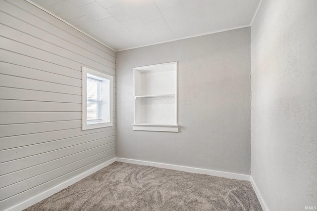 carpeted spare room featuring crown molding and wood walls