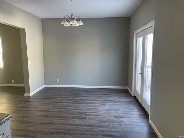 spare room featuring dark wood-type flooring and a chandelier