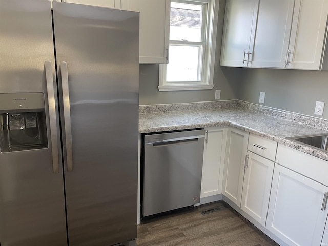 kitchen with appliances with stainless steel finishes, dark hardwood / wood-style flooring, light stone countertops, white cabinets, and sink