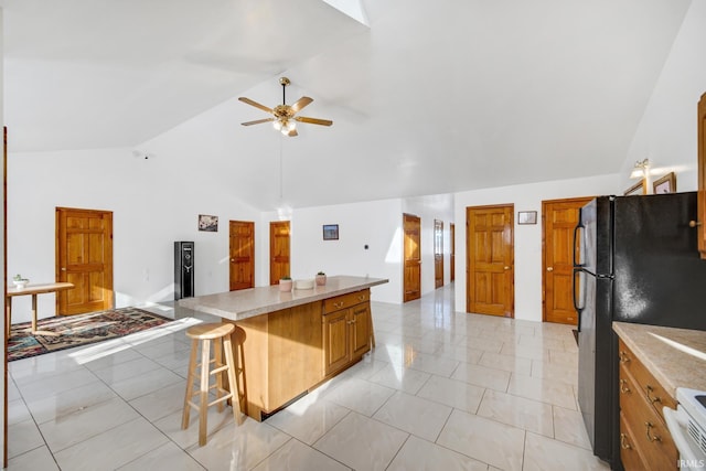 kitchen featuring lofted ceiling, a kitchen bar, black refrigerator, ceiling fan, and stove