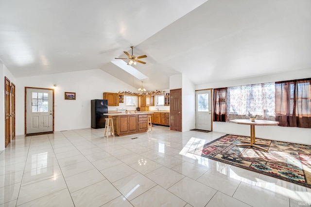 kitchen with ceiling fan, black fridge, a kitchen breakfast bar, vaulted ceiling, and a center island