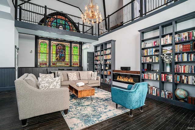 living room with a high ceiling, an inviting chandelier, a wall unit AC, and hardwood / wood-style floors