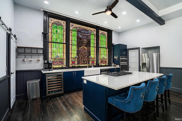 kitchen with wine cooler, a barn door, a center island, beamed ceiling, and appliances with stainless steel finishes