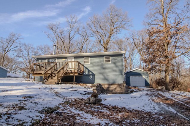 snow covered rear of property featuring a garage, a wooden deck, and an outdoor structure