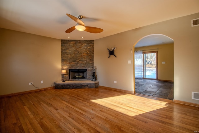 unfurnished living room featuring ceiling fan, a stone fireplace, and hardwood / wood-style flooring