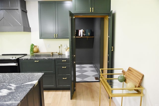 kitchen featuring wall chimney range hood, black / electric stove, dark stone countertops, and light hardwood / wood-style floors