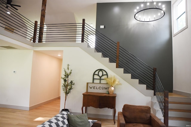 staircase with a towering ceiling, ceiling fan with notable chandelier, and hardwood / wood-style flooring