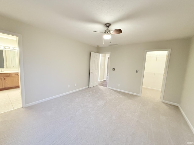 interior space featuring a spacious closet, ensuite bath, a closet, ceiling fan, and light colored carpet