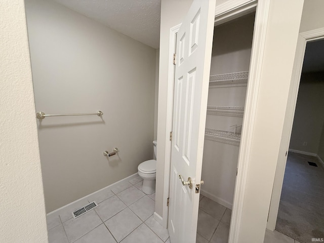 bathroom with a textured ceiling, toilet, and tile patterned flooring