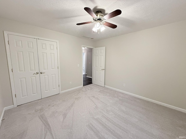 unfurnished bedroom featuring ceiling fan, a closet, light carpet, and a textured ceiling