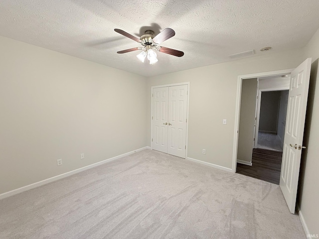 unfurnished bedroom with light carpet, ceiling fan, a closet, and a textured ceiling