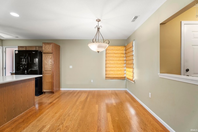 kitchen featuring light hardwood / wood-style floors, hanging light fixtures, and black fridge