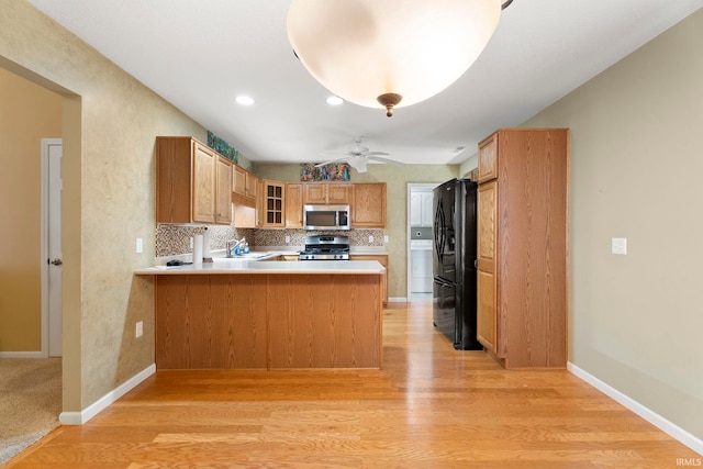 kitchen with kitchen peninsula, appliances with stainless steel finishes, tasteful backsplash, light hardwood / wood-style flooring, and sink