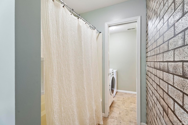 washroom featuring brick wall and separate washer and dryer