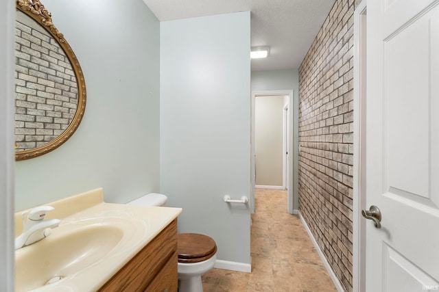 bathroom with toilet, vanity, brick wall, and a textured ceiling