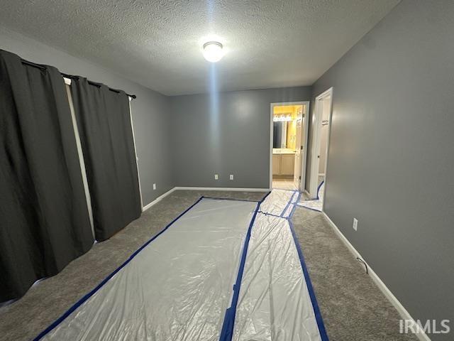 unfurnished bedroom with a textured ceiling, carpet floors, and ensuite bath