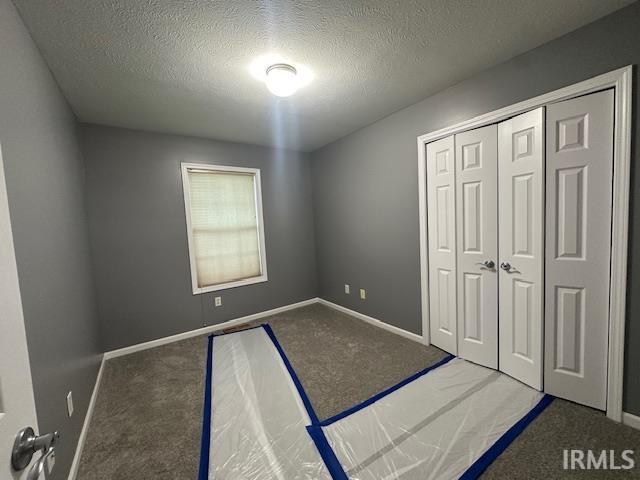 unfurnished bedroom featuring a closet, dark carpet, and a textured ceiling