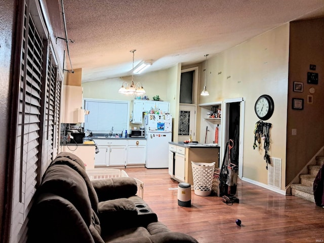 living room with light hardwood / wood-style floors, a textured ceiling, an inviting chandelier, and vaulted ceiling