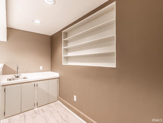 clothes washing area with built in features, light hardwood / wood-style flooring, and sink