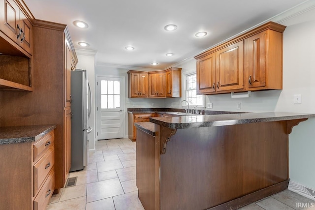 kitchen featuring a breakfast bar, kitchen peninsula, stainless steel fridge, and ornamental molding