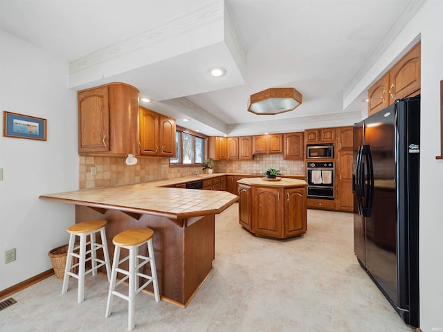 kitchen featuring black appliances, a breakfast bar, kitchen peninsula, crown molding, and a tray ceiling