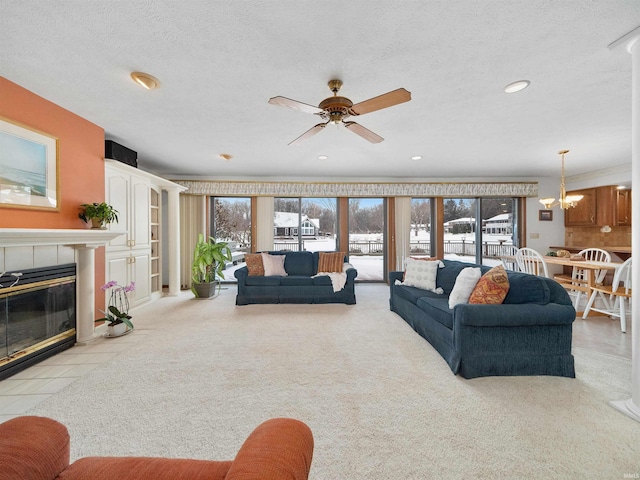 tiled living room featuring a fireplace, ceiling fan with notable chandelier, and a textured ceiling