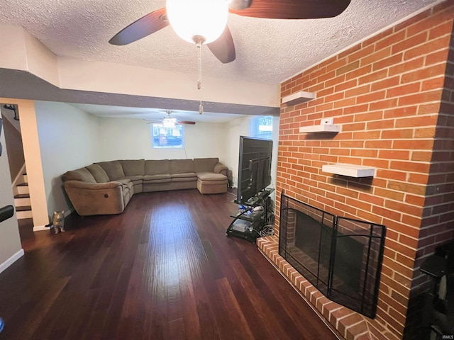 living room featuring ceiling fan, a fireplace, dark hardwood / wood-style flooring, and a textured ceiling