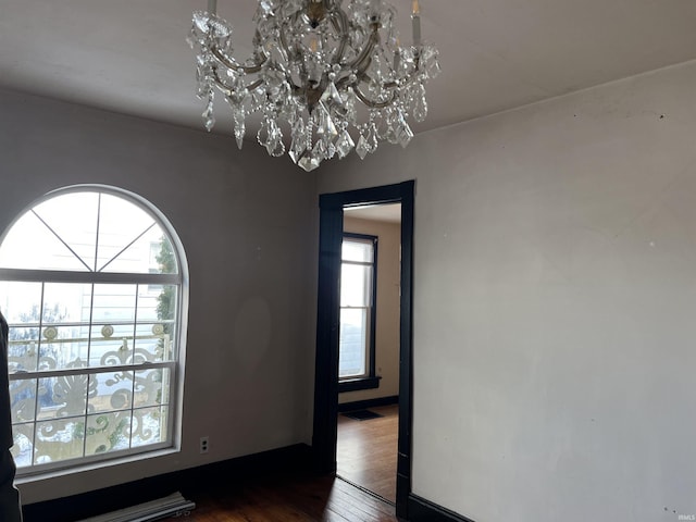 empty room featuring dark wood-type flooring and a notable chandelier