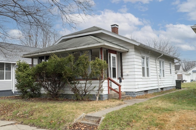 view of side of property with a yard, a shingled roof, and a chimney