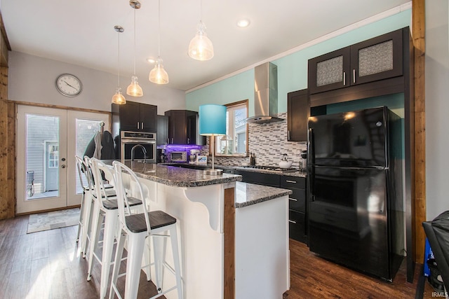 kitchen with pendant lighting, a kitchen island with sink, appliances with stainless steel finishes, a kitchen breakfast bar, and wall chimney exhaust hood