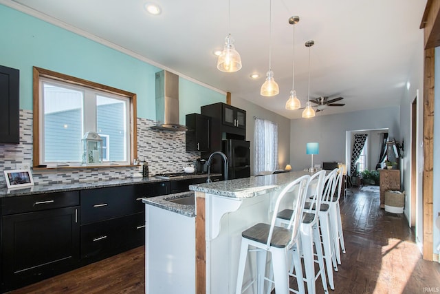 kitchen featuring black refrigerator, an island with sink, a breakfast bar area, wall chimney exhaust hood, and sink