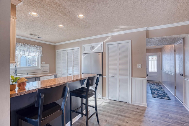 kitchen with plenty of natural light, sink, stainless steel refrigerator, a breakfast bar, and crown molding