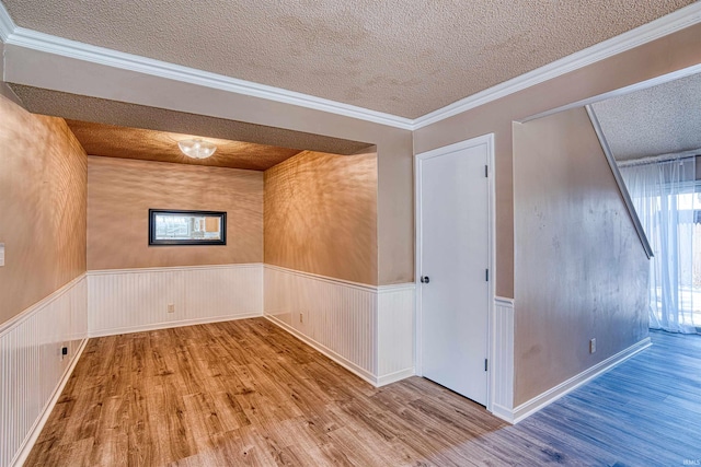 empty room with a textured ceiling, ornamental molding, and hardwood / wood-style floors