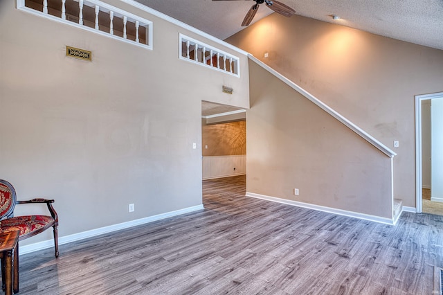 unfurnished living room with ceiling fan, high vaulted ceiling, a textured ceiling, and light hardwood / wood-style flooring