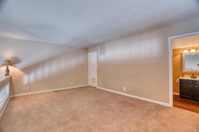 unfurnished room featuring light carpet, sink, and a textured ceiling