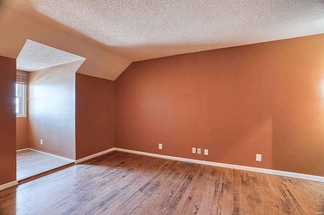 additional living space with vaulted ceiling, a textured ceiling, and hardwood / wood-style floors