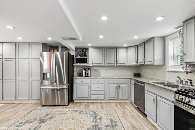 kitchen with light stone countertops, gray cabinetry, stainless steel appliances, and light hardwood / wood-style flooring