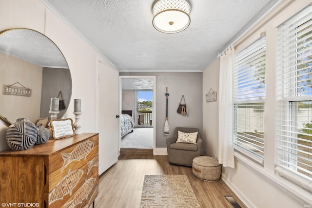 interior space featuring light wood-type flooring, ornamental molding, and a textured ceiling