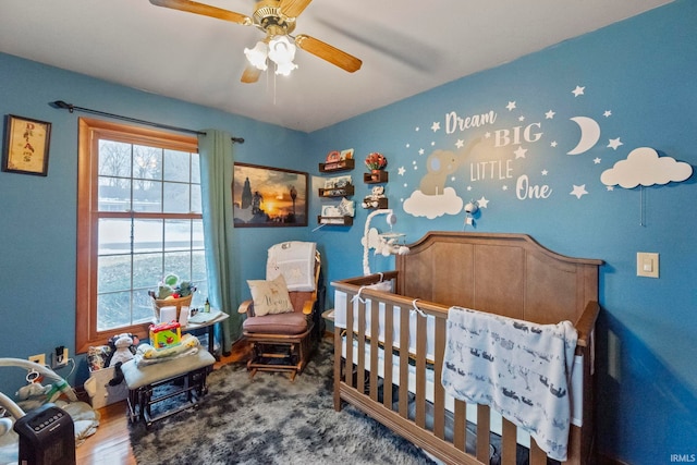 bedroom with ceiling fan, hardwood / wood-style floors, and a nursery area